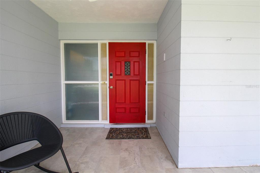 A red front door with side windows sits on a covered porch with tiled flooring — 2521 BISMARK WAY, SARASOTA, FL