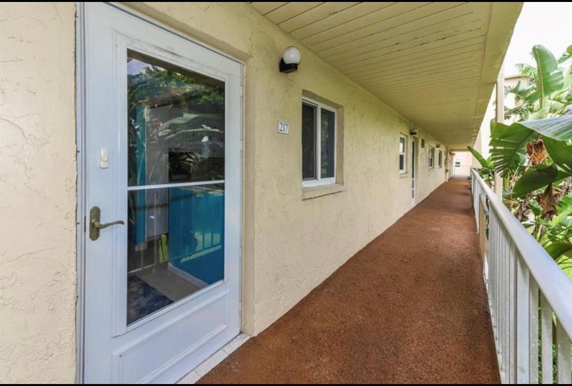 An exterior view of a building walkway featuring a white door labeled 217 — 2615 NE 3rd Court # 217, Boynton Beach FL 33435, BOYNTON BEACH, FL