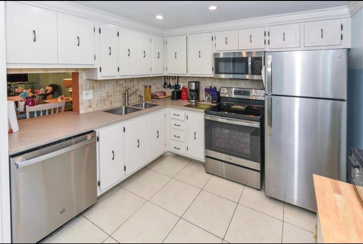 A kitchen features white cabinetry, stainless steel appliances, a tiled backsplash, and light-colored floor tiles — 2615 NE 3rd Court # 217, Boynton Beach FL 33435, BOYNTON BEACH, FL