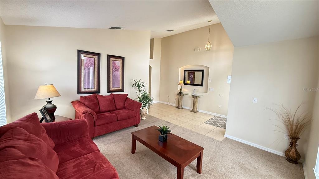 A living room features red sofas, a coffee table, and a tiled entryway with an alcove — 7979 MAGNOLIA BEND COURT, KISSIMMEE, FL