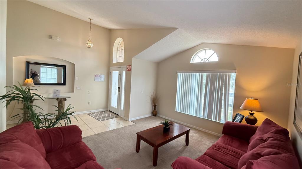 A living room features vaulted ceilings, two red sofas, a coffee table, and an entryway — 7979 MAGNOLIA BEND COURT, KISSIMMEE, FL