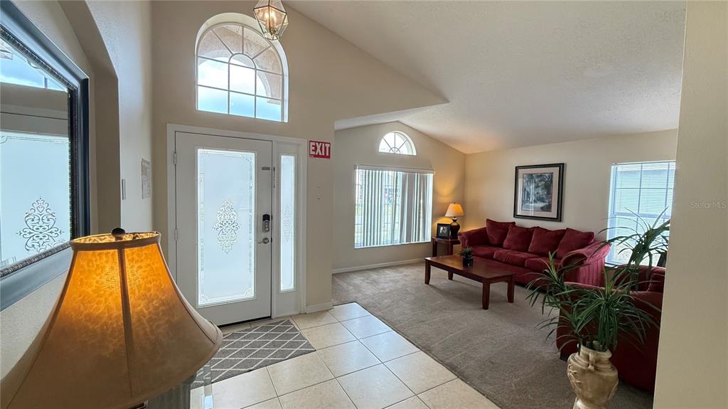 A living room features a tiled entryway, carpeted seating area, vaulted ceilings, and a front door — 7979 MAGNOLIA BEND COURT, KISSIMMEE, FL