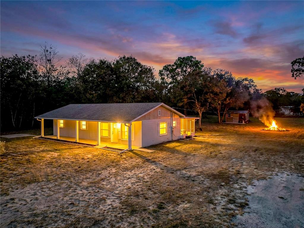 A single-story house with a porch and a bonfire in the yard at sunset — 9421 SUNSHINE GROVE ROAD, BROOKSVILLE, FL