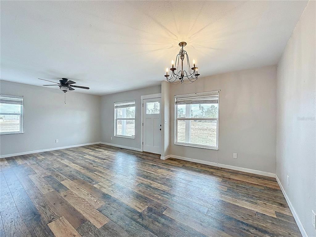 An empty living room features wood-look flooring, a ceiling fan, and a decorative chandelier — 9421 SUNSHINE GROVE ROAD, BROOKSVILLE, FL