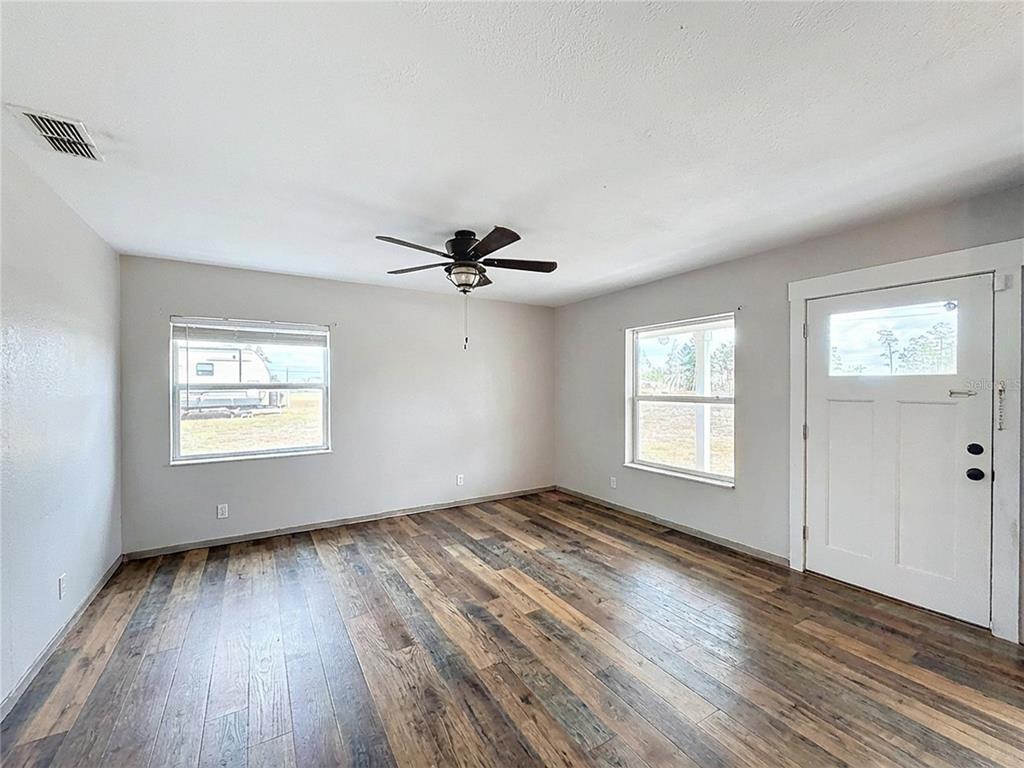 An empty room features wood-look flooring, a ceiling fan, two windows, and a white door — 9421 SUNSHINE GROVE ROAD, BROOKSVILLE, FL