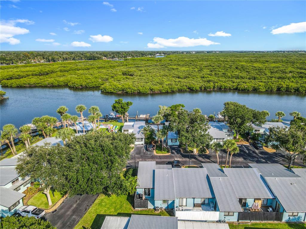 An aerial view shows a waterfront residential complex with metal roofs and surrounding trees — 85 HEATHER POINT COURT UNIT 850, NEW SMYRNA BEACH, FL