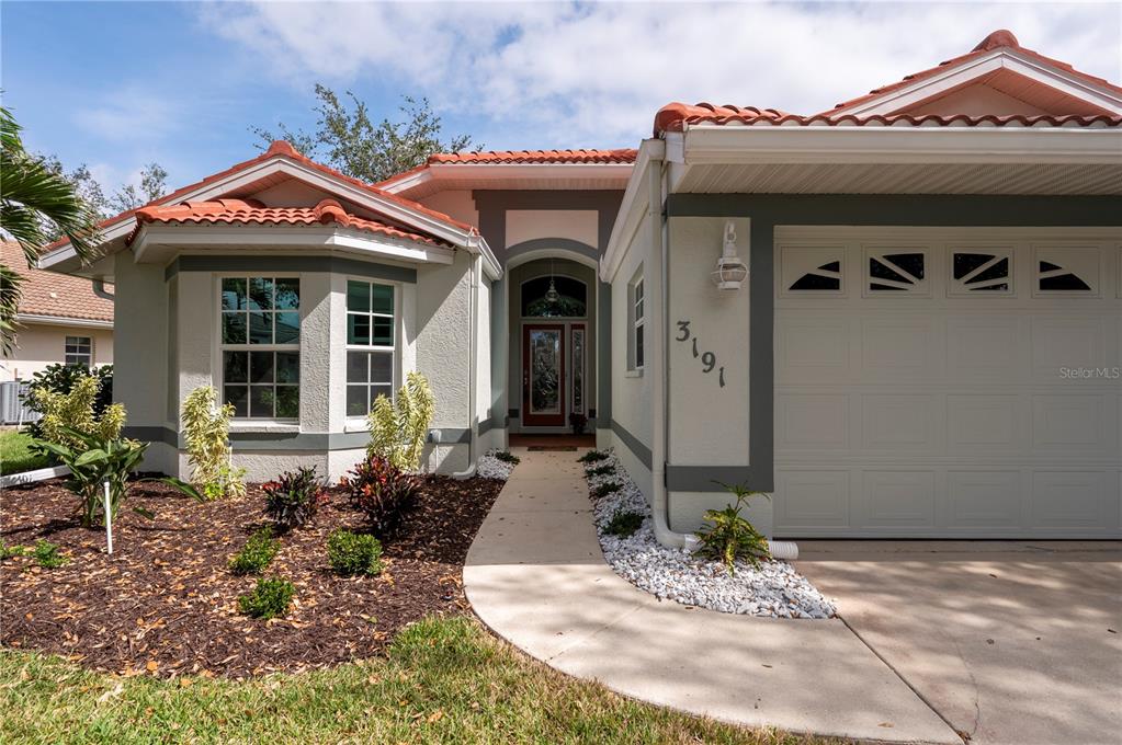 The exterior of a single-story house features a tiled roof, stucco walls, and a driveway — 3191 VILLAGE LANE, PORT CHARLOTTE, FL