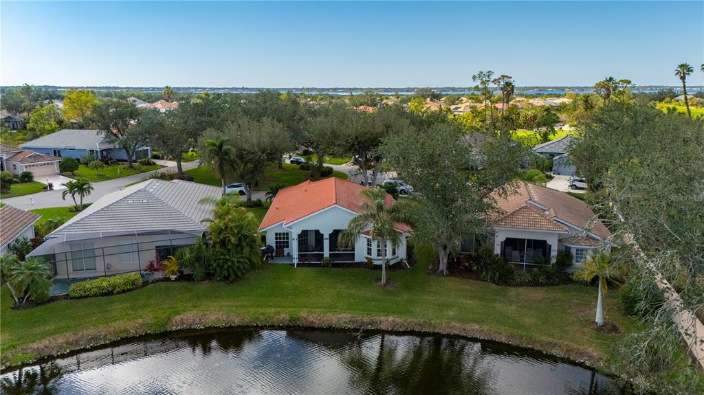 An aerial view shows three suburban houses with tiled roofs situated along a small pond — 3191 VILLAGE LANE, PORT CHARLOTTE, FL