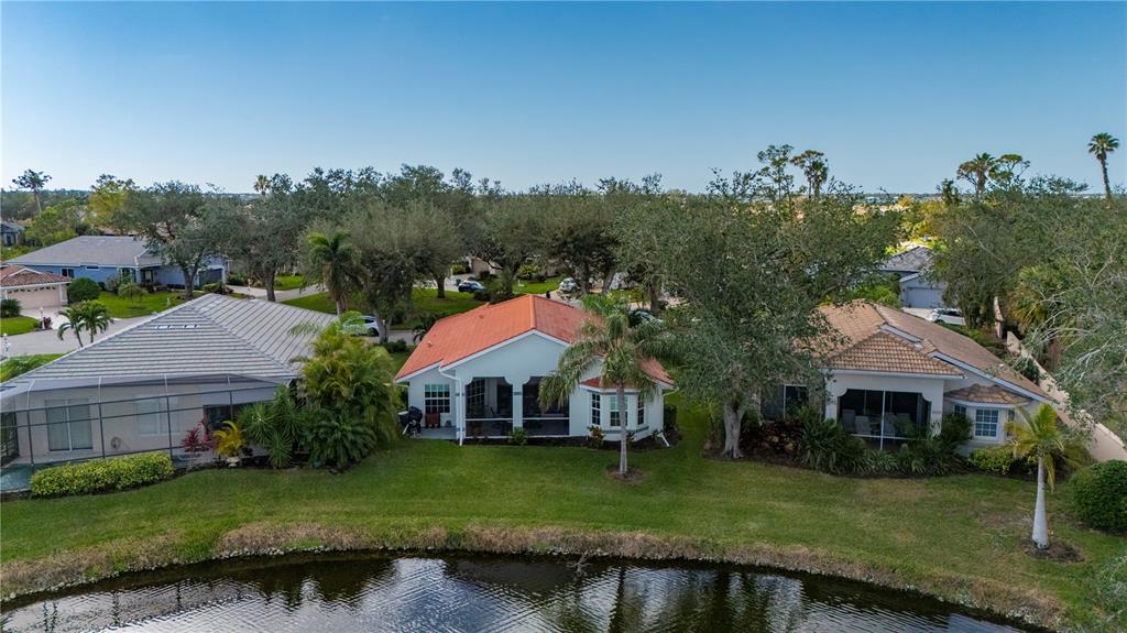 An aerial view shows three houses with screened lanais situated along a small pond — 3191 VILLAGE LANE, PORT CHARLOTTE, FL