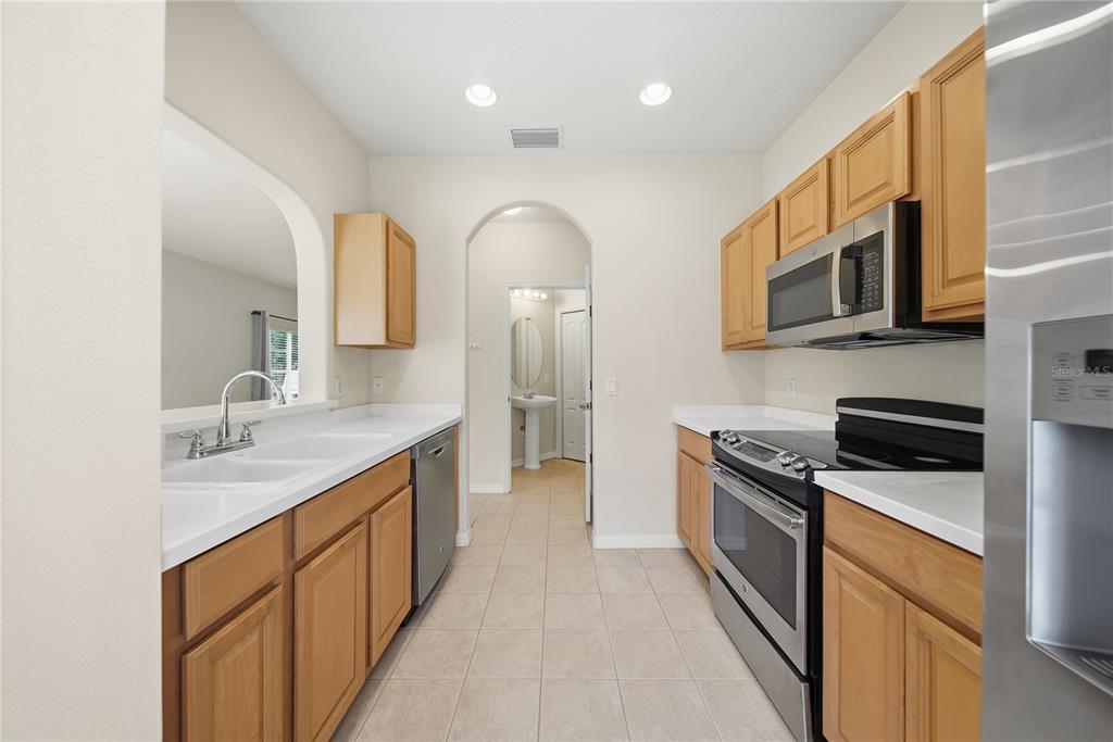 A galley kitchen features light wood cabinets, white countertops, stainless steel appliances, and tile flooring — 335 CAPE HARBOUR LOOP UNIT 108, BRADENTON, FL