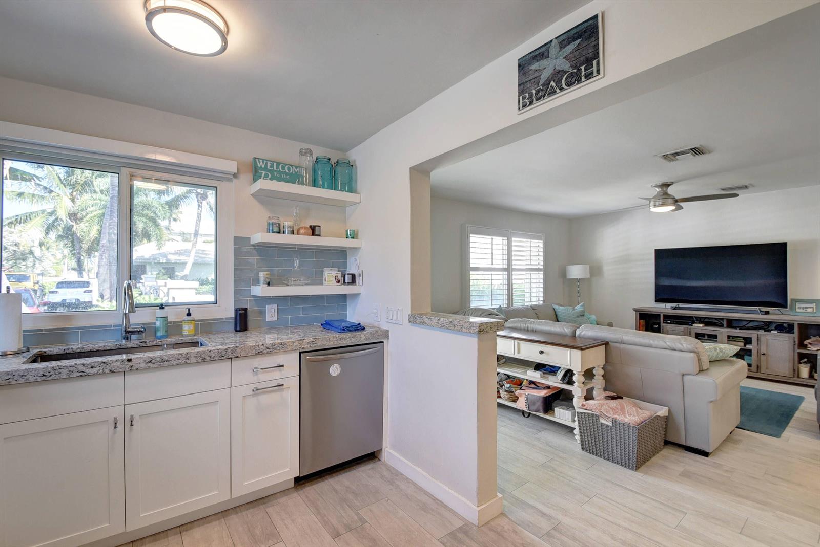 A kitchen with white cabinets and granite countertops opens into a living room with a television — 1020 Casuarina Road, Delray Beach FL 33483, DELRAY BEACH, FL