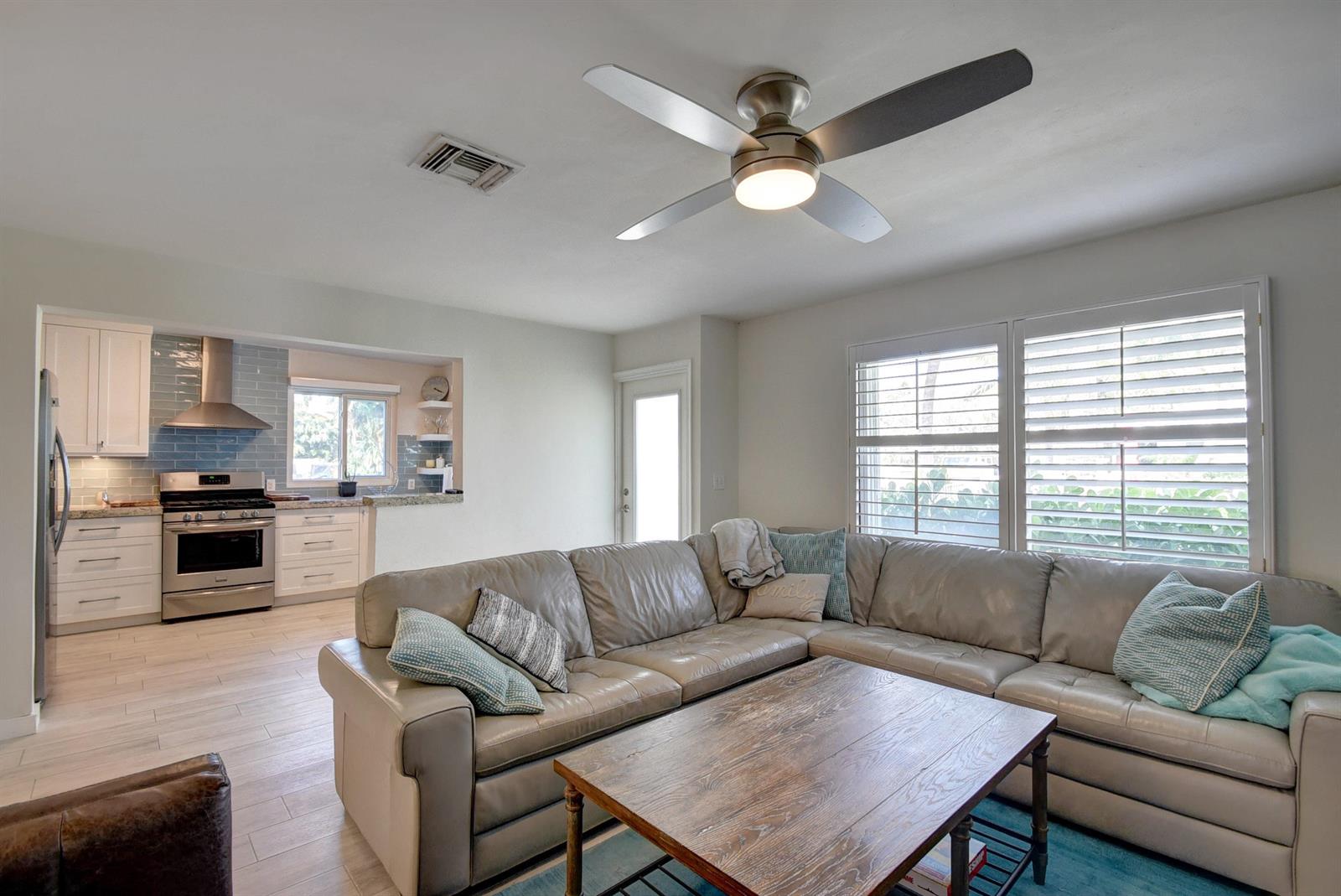 A living room with a sectional sofa and coffee table opens to a modern kitchen — 1020 Casuarina Road, Delray Beach FL 33483, DELRAY BEACH, FL
