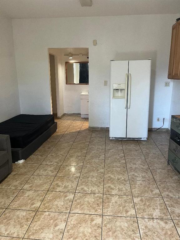 A room with tiled flooring, a bed, and a white refrigerator leads to a bathroom — 8421 S ORANGE BLOSSOM TRAIL UNIT 254, ORLANDO, FL