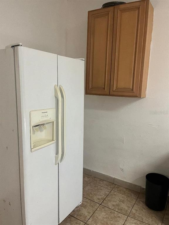 A white side-by-side refrigerator sits next to a wooden wall cabinet in a tiled kitchen — 8421 S ORANGE BLOSSOM TRAIL UNIT 254, ORLANDO, FL