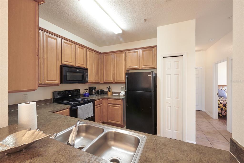 A kitchen with wood cabinets, black appliances, and a double-basin sink on a laminate countertop — 7513 PELLHAM WAY, KISSIMMEE, FL