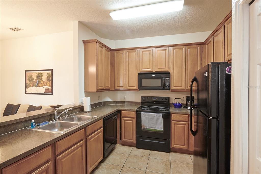 A kitchen features light wood cabinets, black appliances, dark countertops, and tile flooring — 7513 PELLHAM WAY, KISSIMMEE, FL
