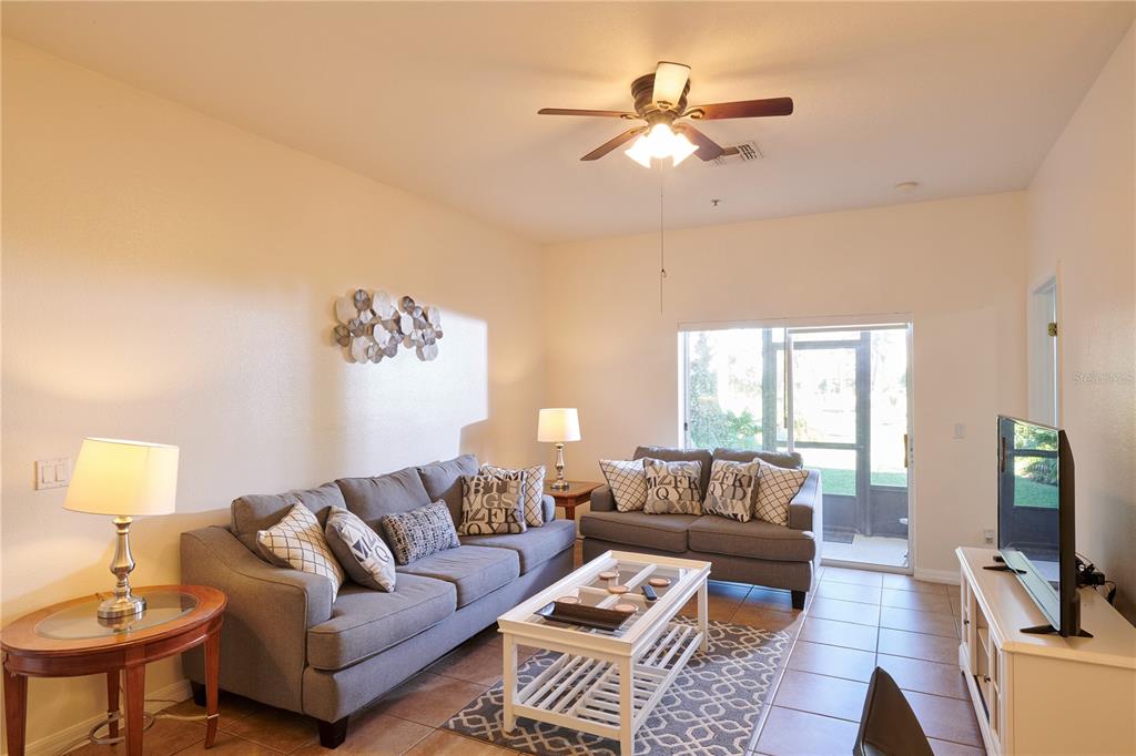 A living room features two gray sofas, a white coffee table, and a ceiling fan — 7513 PELLHAM WAY, KISSIMMEE, FL