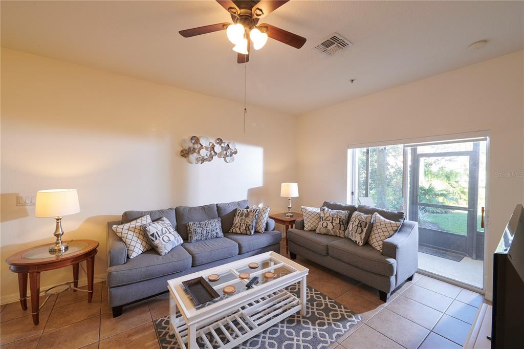 A living room features two gray sofas, a white coffee table, and a sliding glass door — 7513 PELLHAM WAY, KISSIMMEE, FL