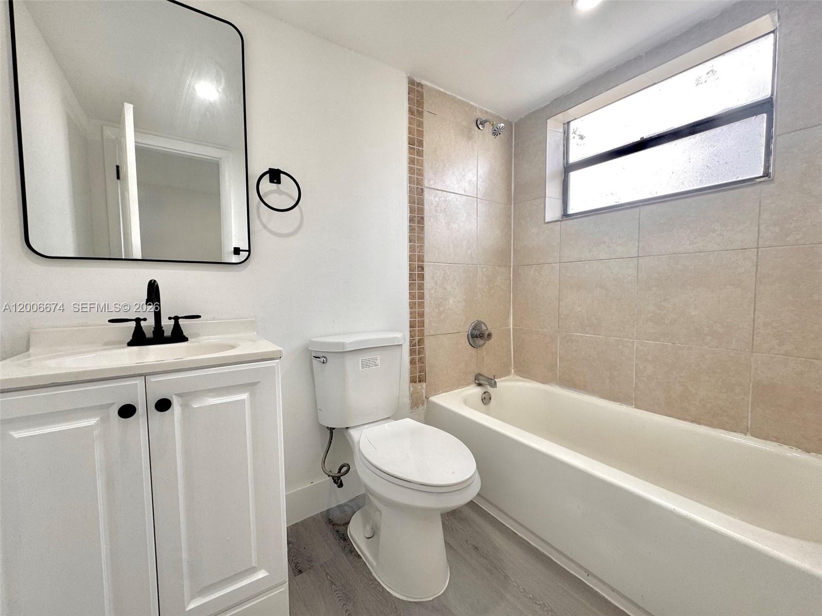 A bathroom features a white vanity, a toilet, and a bathtub with beige tiled walls — 417 NW 2nd Ave # 000, Hallandale Beach FL 33009, HALLANDALE BEACH, FL