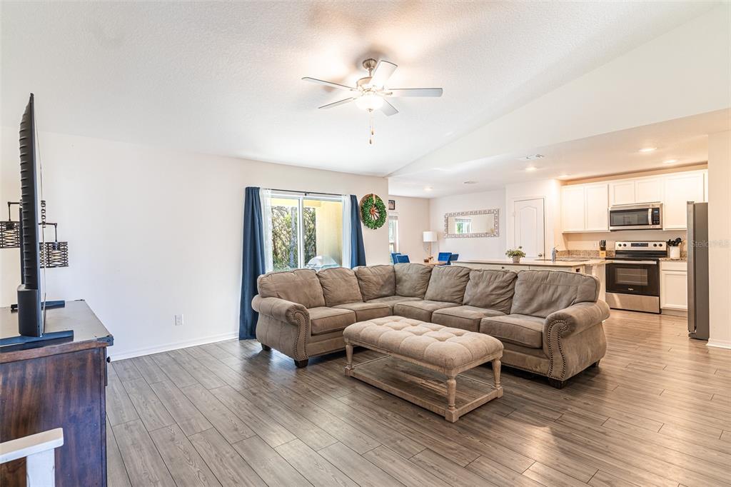 A living room with wood-look flooring features a large sectional sofa and an open kitchen — 437 RIO GRANDE PLACE, POINCIANA, FL