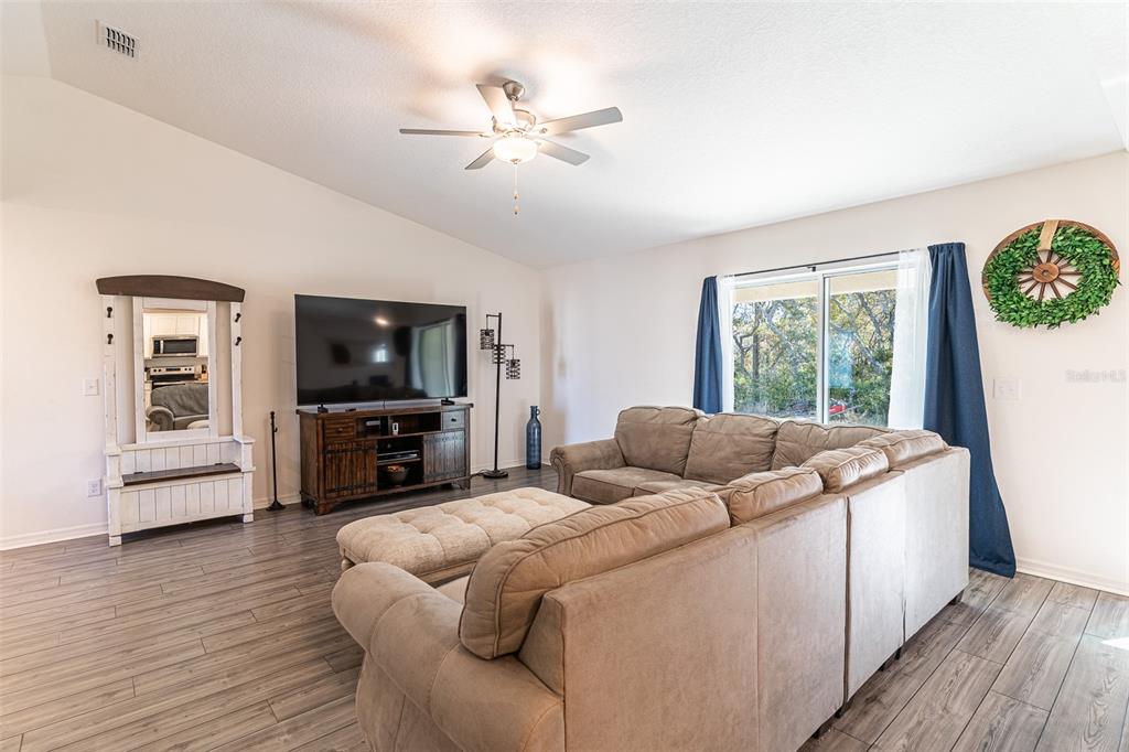 A living room features a sectional sofa, a television on a wooden console, and wood-look flooring — 437 RIO GRANDE PLACE, POINCIANA, FL
