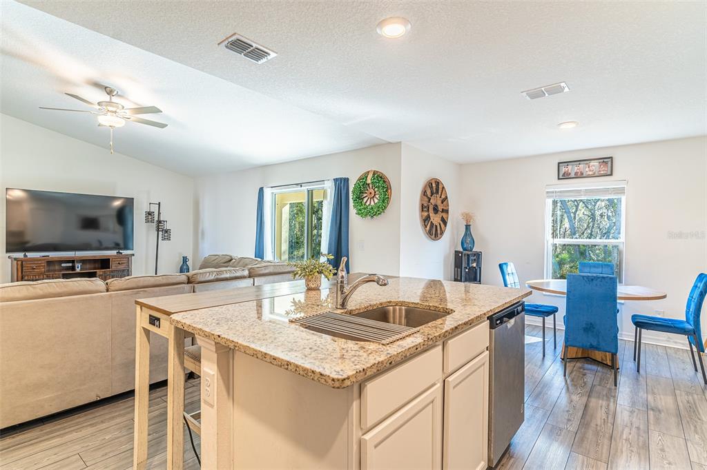 A kitchen island with granite countertops sits in front of a living room and dining area — 437 RIO GRANDE PLACE, POINCIANA, FL
