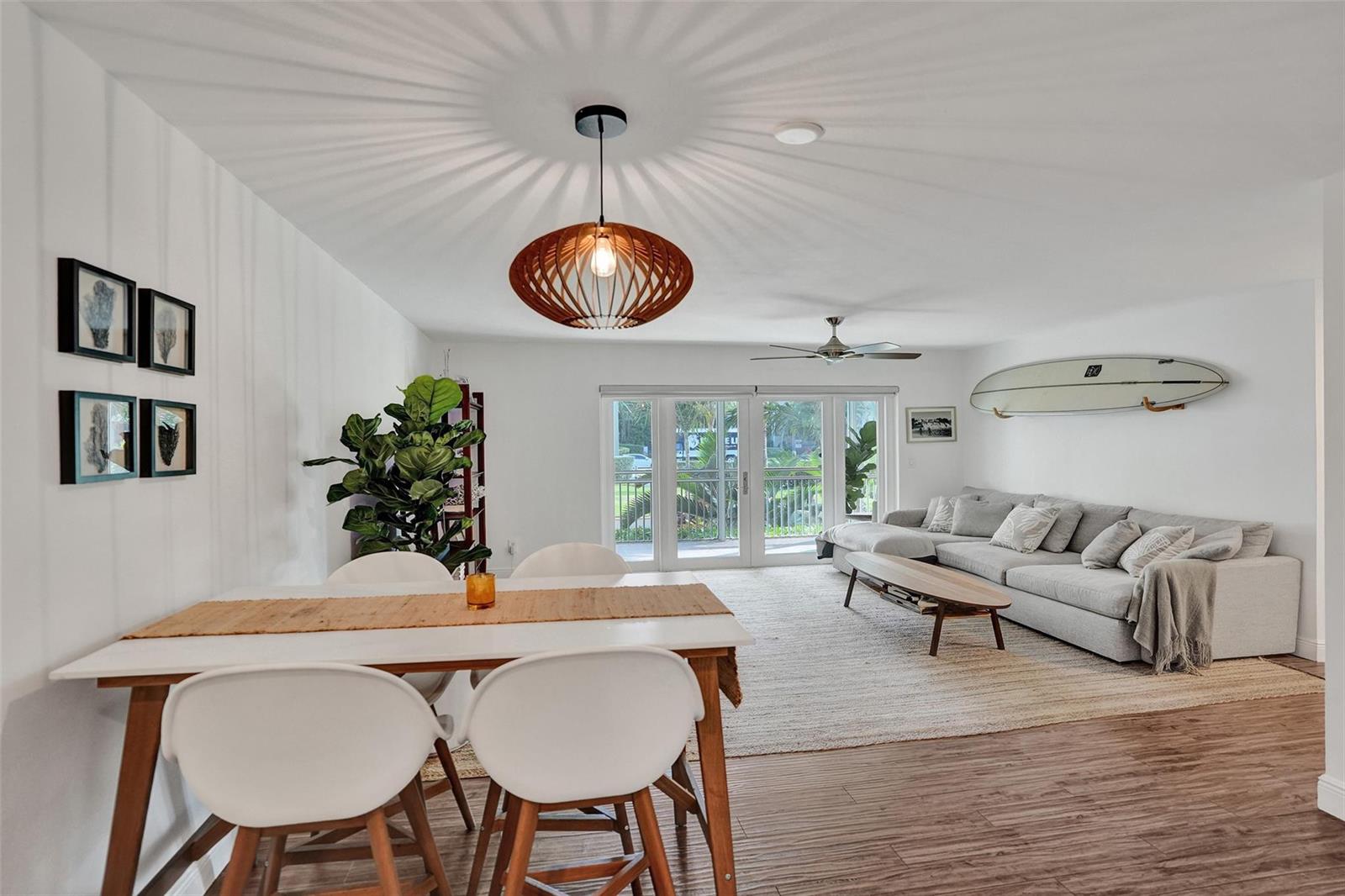A bright living and dining area features a wooden pendant light, surfboard decor, and sofa — 2501 S Ocean Boulevard # 1030, Boca Raton FL 33432, BOCA RATON, FL