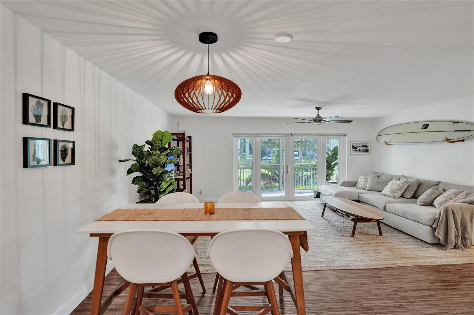 A dining area with a wooden pendant light opens into a living room with a surfboard — 2501 S Ocean Boulevard # 1030, Boca Raton FL 33432, BOCA RATON, FL