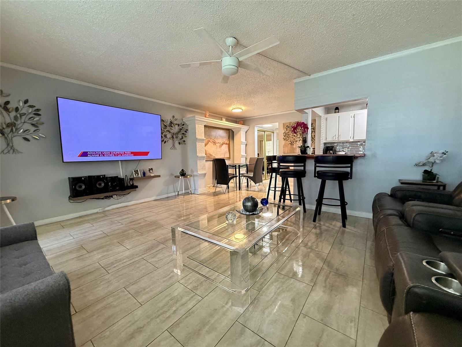 A living room features a large wall-mounted television, a glass coffee table, and bar seating — 355 Oakridge T # 355, Deerfield Beach FL 33442, DEERFIELD BEACH, FL