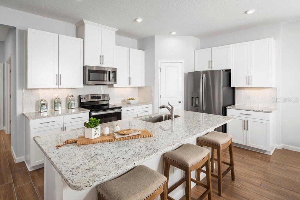 A modern kitchen features white cabinets, granite countertops, stainless steel appliances, and a central island — 2207 GREAT EGRET CIRCLE, OCOEE, FL
