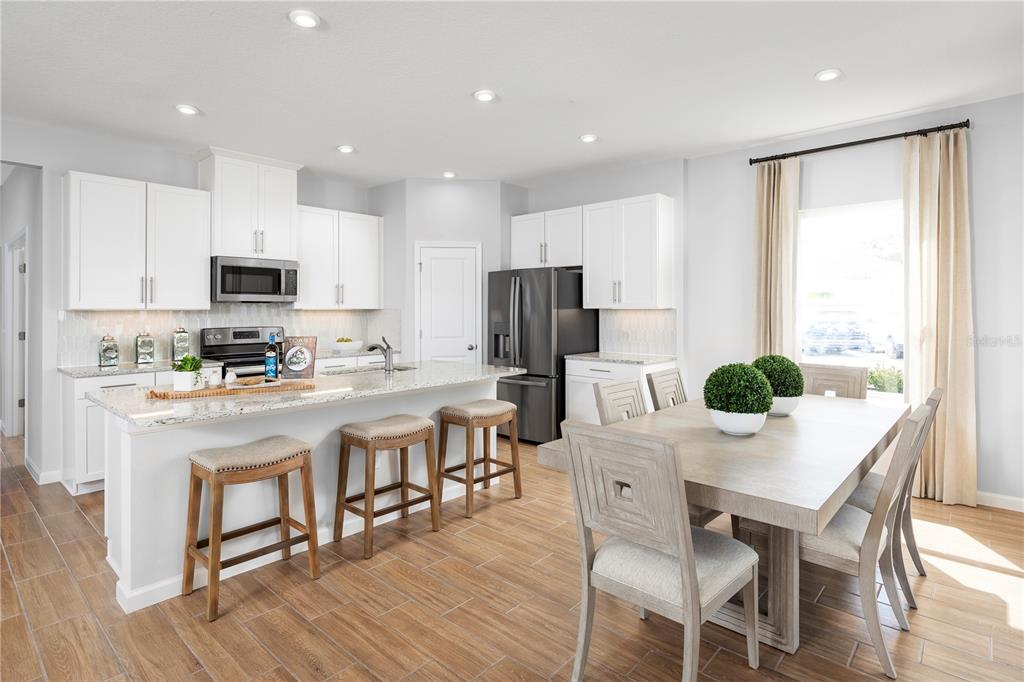 A modern kitchen features white cabinetry, granite countertops, a center island, and an adjacent dining area — 2207 GREAT EGRET CIRCLE, OCOEE, FL