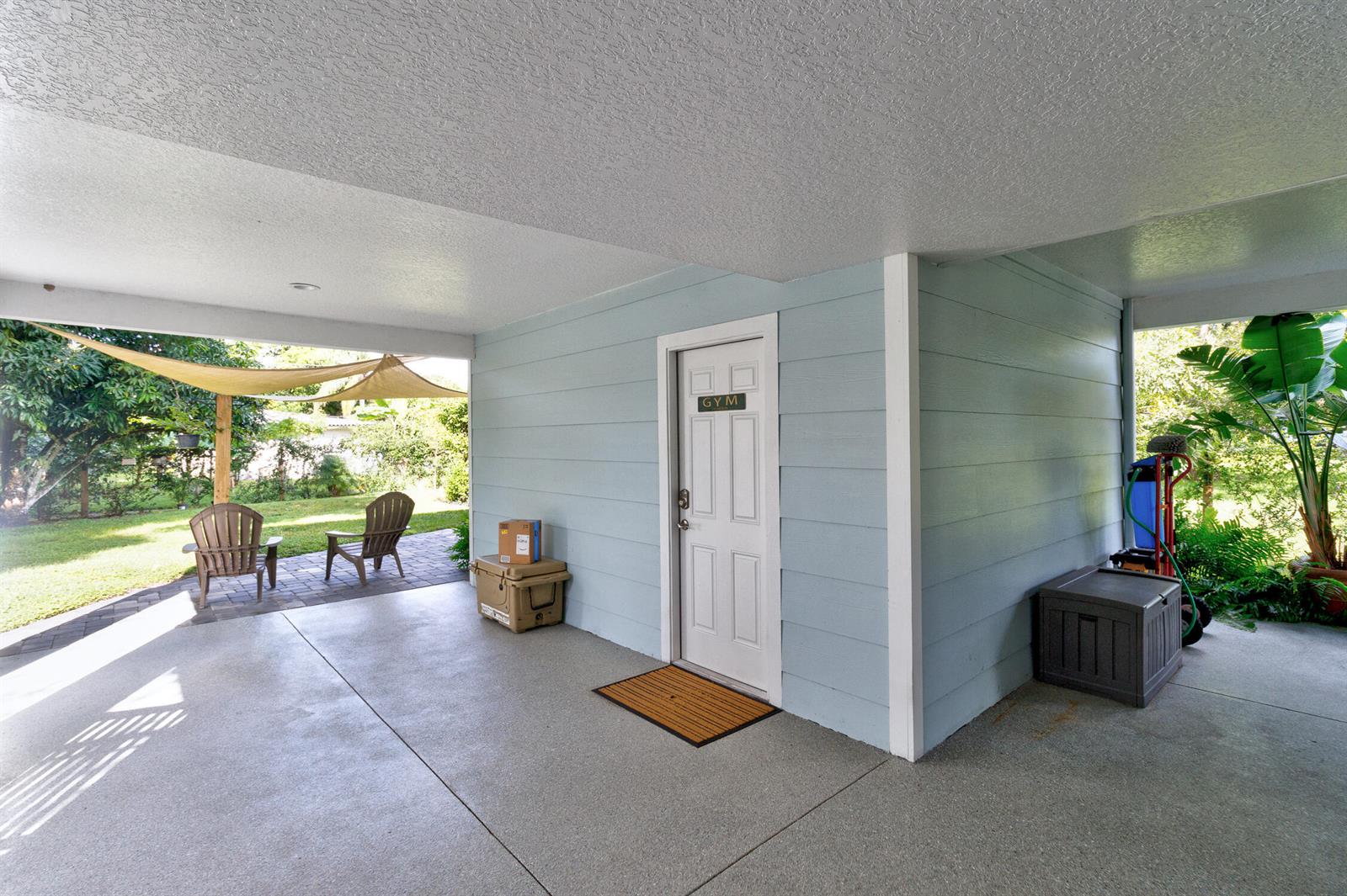 A covered patio features a light blue wall, a gym door, and outdoor seating — FELLSMERE, FL