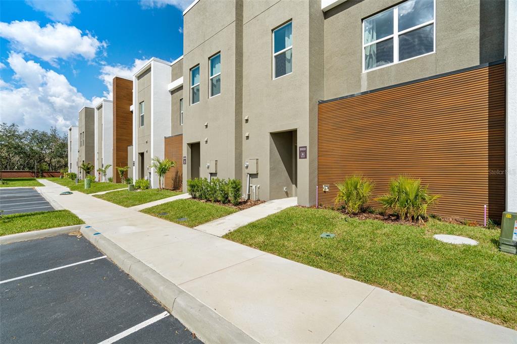 A row of modern townhomes with tan stucco, wood-slat siding, and a concrete sidewalk — 9084 BORACAY COURT, KISSIMMEE, FL