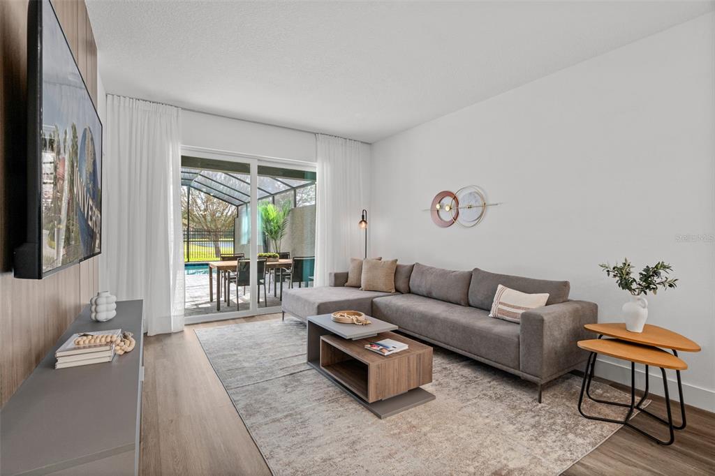 A modern living room features a gray sectional sofa, wood coffee table, and sliding glass doors — 9084 BORACAY COURT, KISSIMMEE, FL