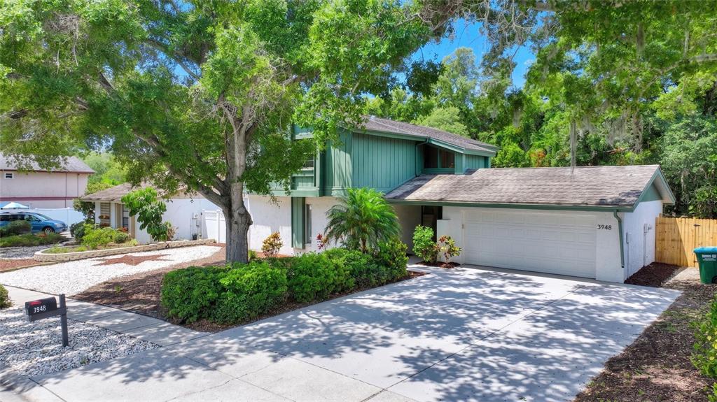 A two-story house with green vertical siding, a white garage, and a large front tree — 3948 ORCHARD HILL CIRCLE, PALM HARBOR, FL