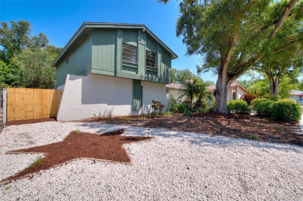 A two-story house with green siding and white stucco features a star-shaped mulch garden bed — 3948 ORCHARD HILL CIRCLE, PALM HARBOR, FL