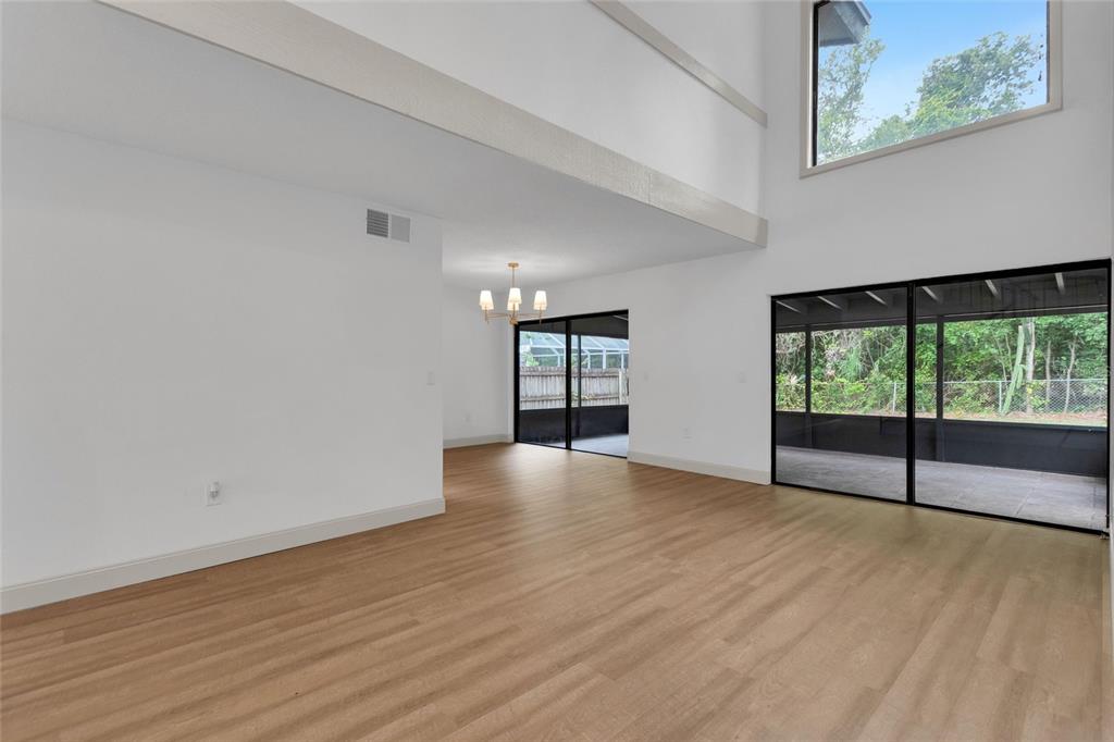 A bright living area features high ceilings, light wood-look flooring, and large sliding glass doors — 3948 ORCHARD HILL CIRCLE, PALM HARBOR, FL