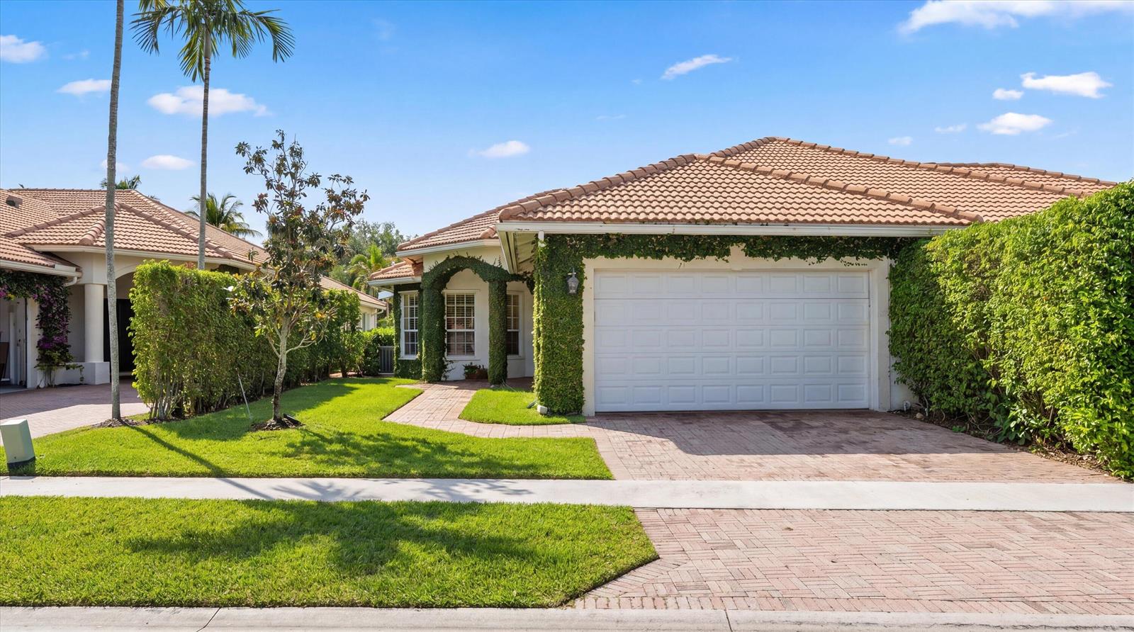 A single-story house with a white garage, tiled roof, and ivy-covered walls near a lawn — 2920 Twin Oaks Way, Wellington FL 33414, WELLINGTON, FL