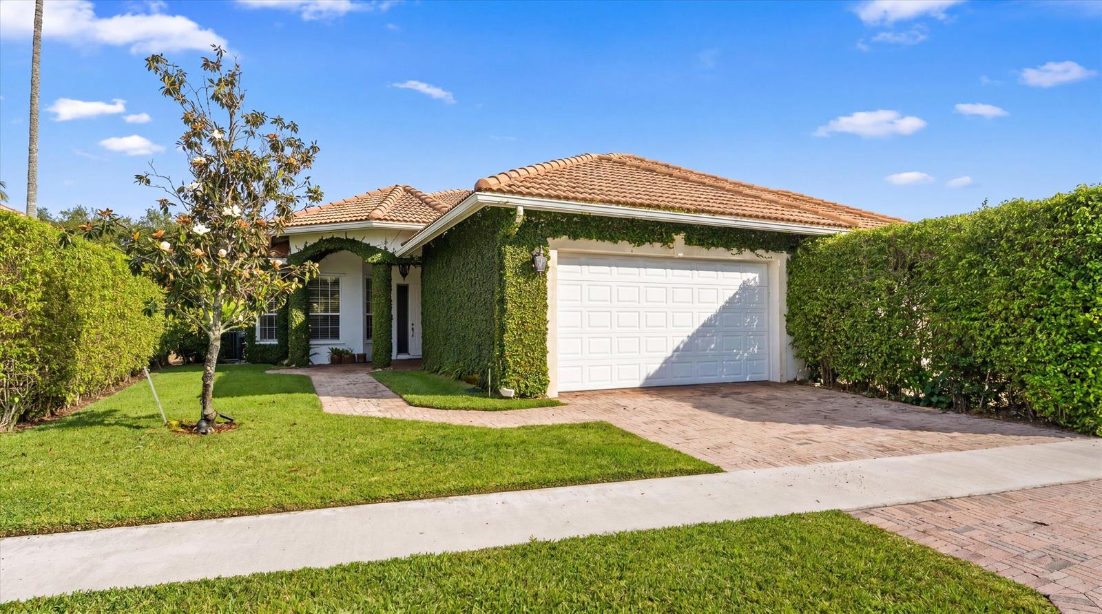 A single-story house with a tiled roof, a two-car garage, and walls covered in ivy — 2920 Twin Oaks Way, Wellington FL 33414, WELLINGTON, FL