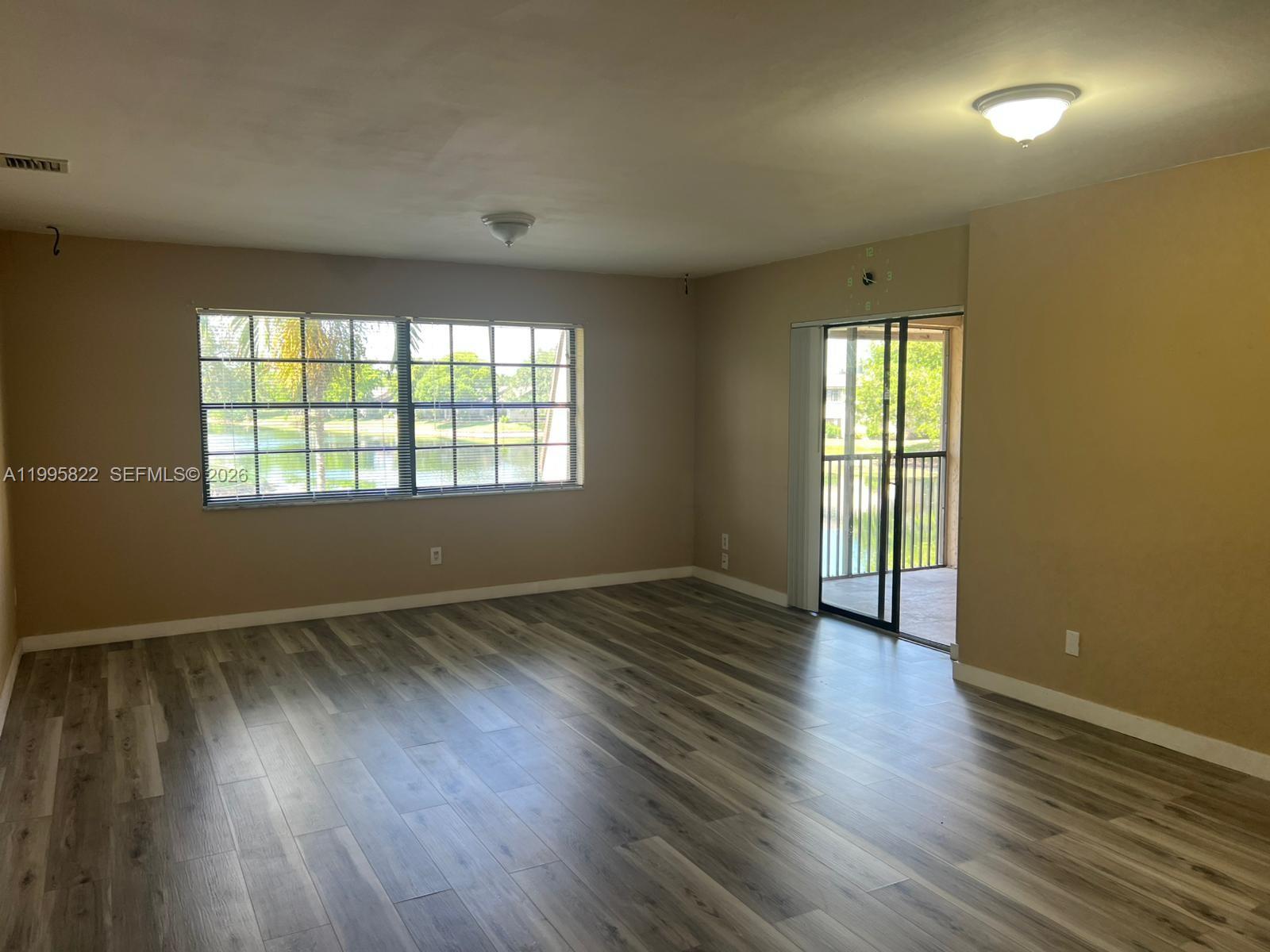 An empty living room features wood-look flooring, beige walls, a large window, and a sliding door — 3655 NW 94th Ave # 8H, Sunrise FL 33351, SUNRISE, FL