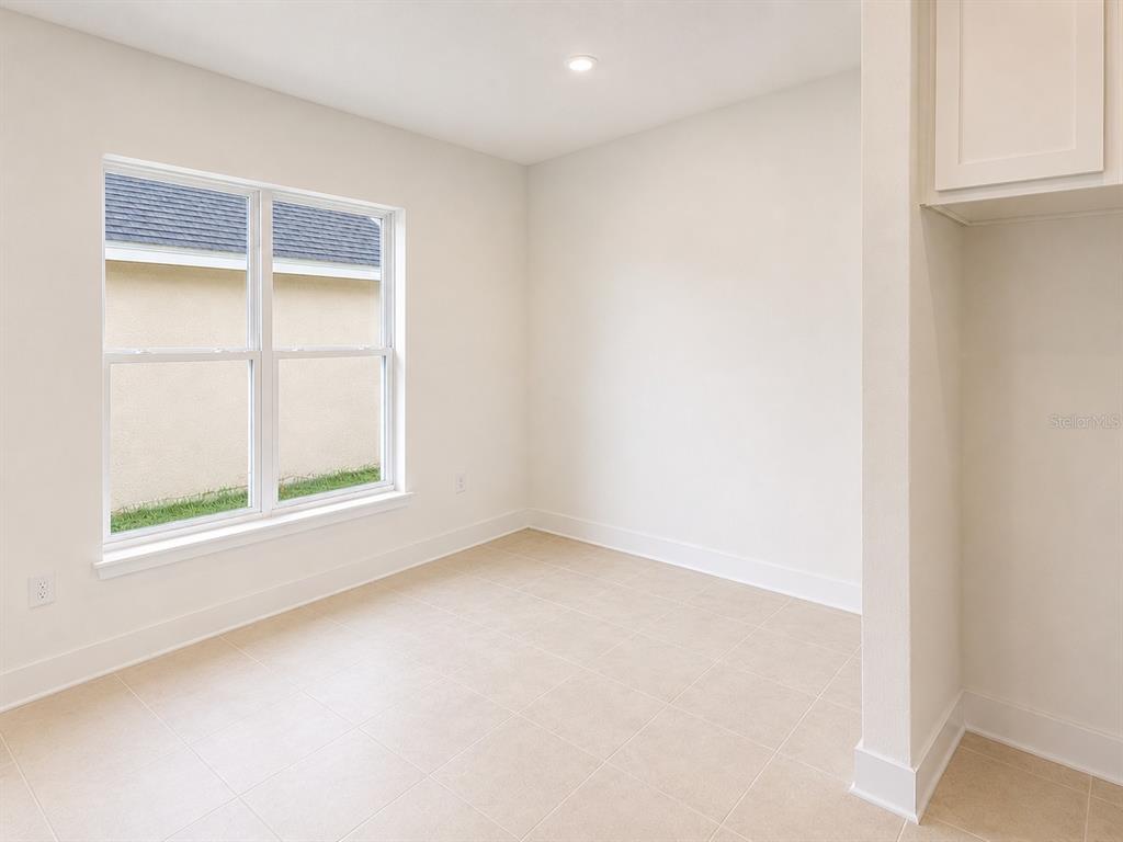 An empty room with beige tile flooring, white walls, and a large window — 1639 ANN ROSE WAY, LEESBURG, FL