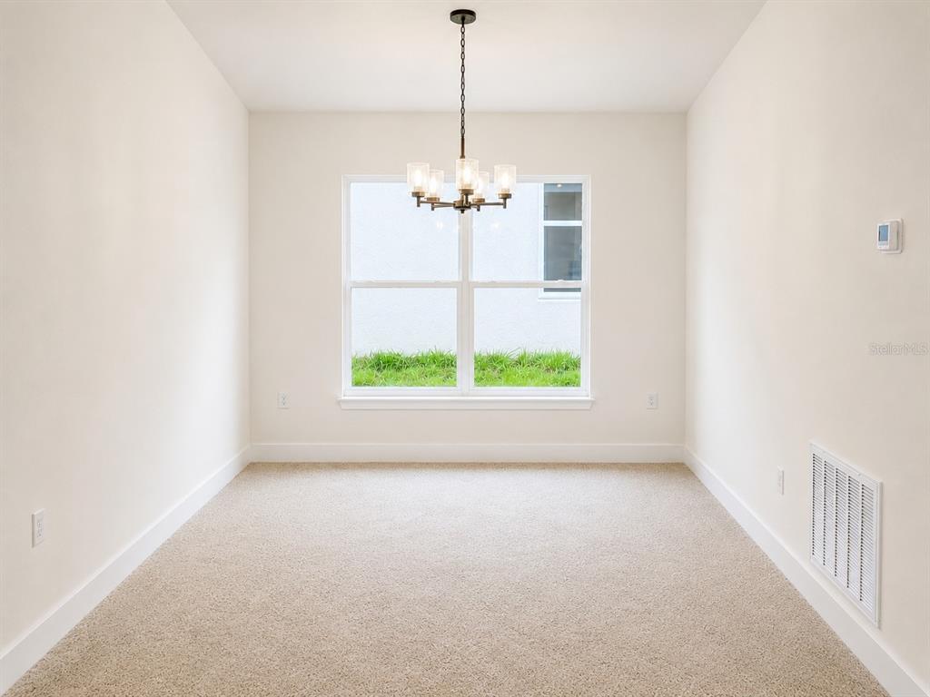 A dining room features beige carpet, white walls, a central chandelier, and a large window — 1639 ANN ROSE WAY, LEESBURG, FL