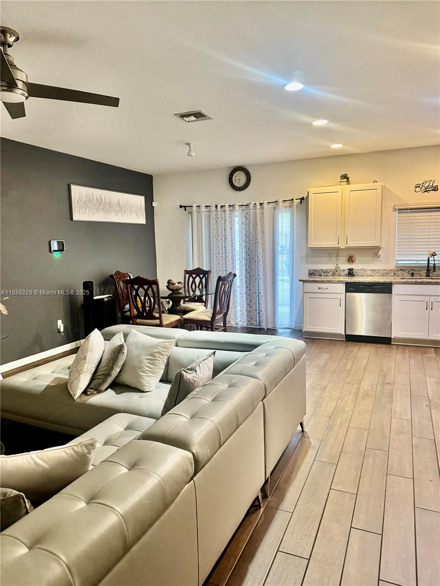 This open-concept living and dining area features a large sectional sofa and white kitchen cabinetry — 4039 NW 11th St, Lauderhill FL 33313, LAUDERHILL, FL