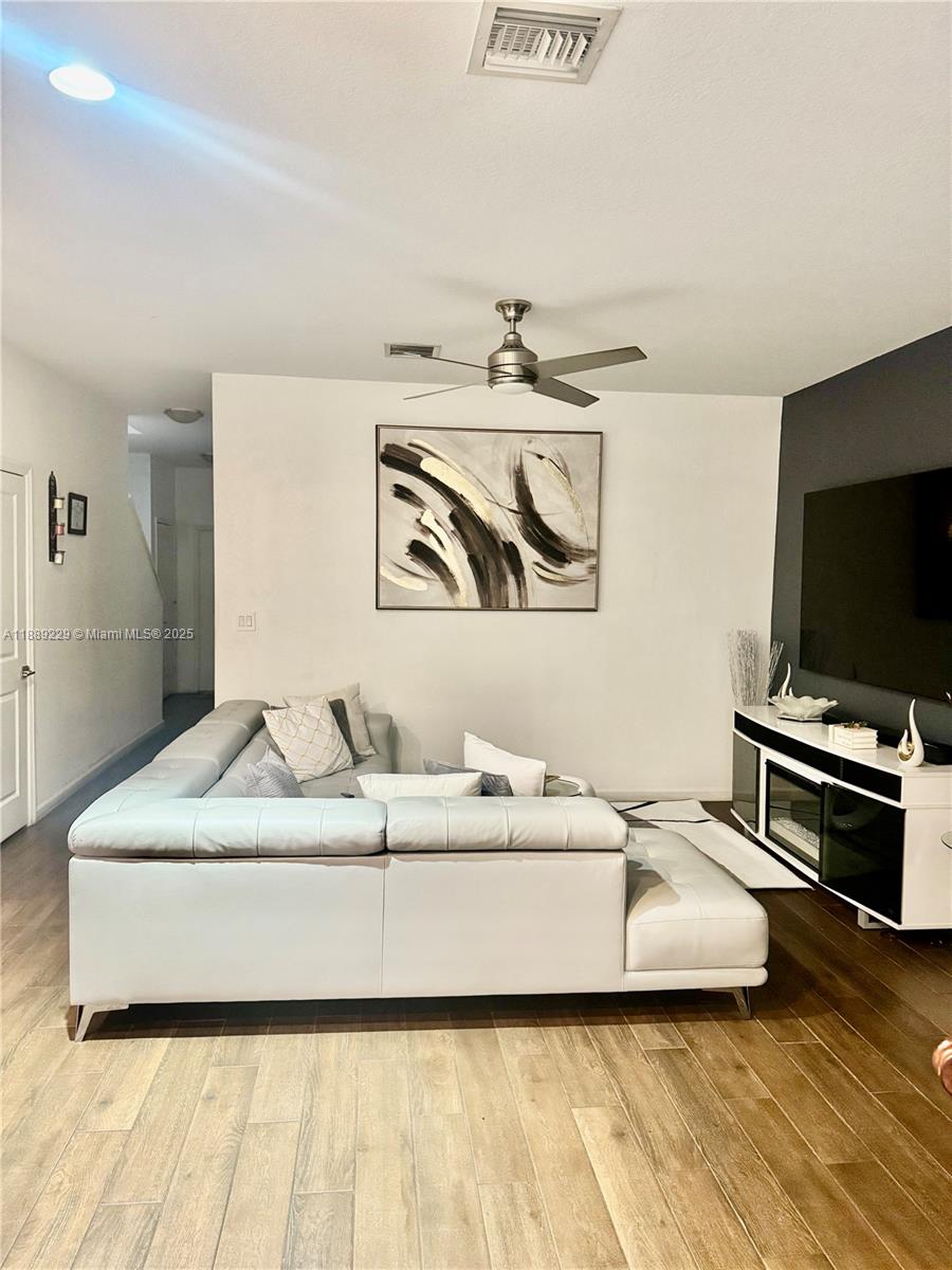 A living room features a white sectional sofa, a wall-mounted television, and wood-look flooring — 4039 NW 11th St, Lauderhill FL 33313, LAUDERHILL, FL