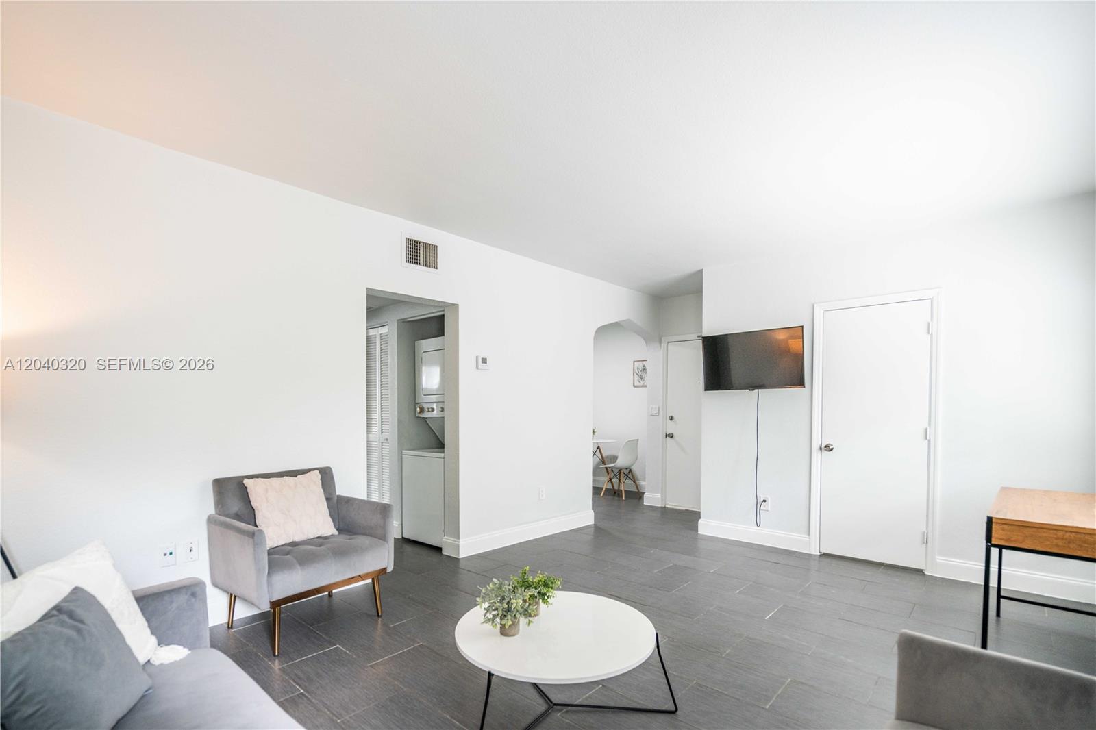A living room features gray tile flooring, a mounted television, and a small laundry closet — 1007 Bay Dr # 104, Miami Beach FL 33141, MIAMI BEACH, FL