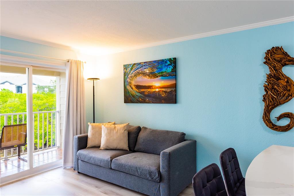 A living room features a gray sofa, a wave-themed wall canvas, and a balcony view — 2506 N ROCKY POINT DRIVE UNIT 275, TAMPA, FL
