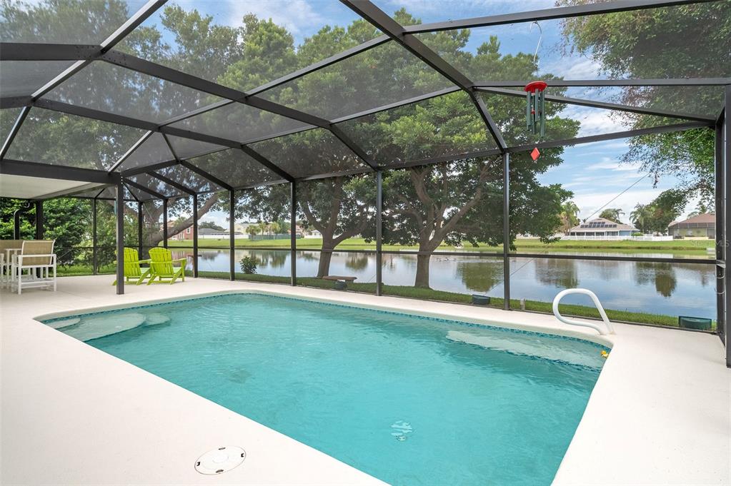 A screened-in swimming pool overlooks a lake with trees and houses in the background — 411 WENTHROP CIRCLE, ROCKLEDGE, FL