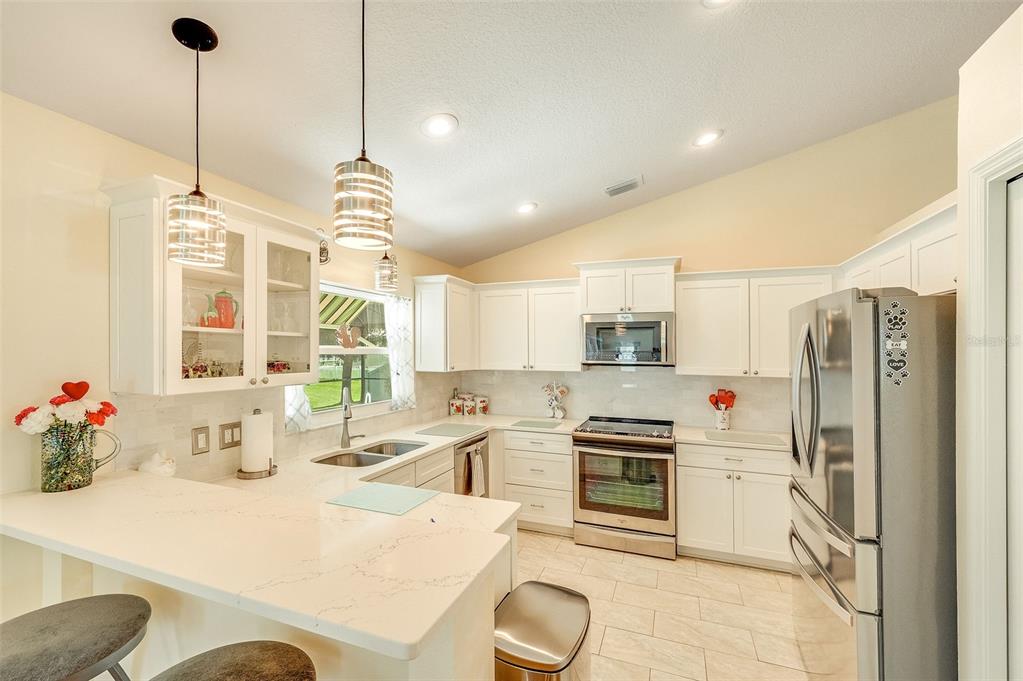 A bright kitchen features white cabinets, stainless steel appliances, and a quartz-topped breakfast bar — 411 WENTHROP CIRCLE, ROCKLEDGE, FL