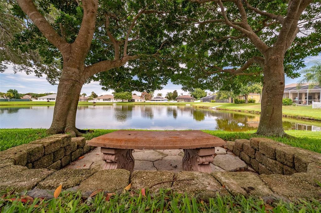 A stone bench sits under two large trees overlooking a calm pond in a backyard — 411 WENTHROP CIRCLE, ROCKLEDGE, FL