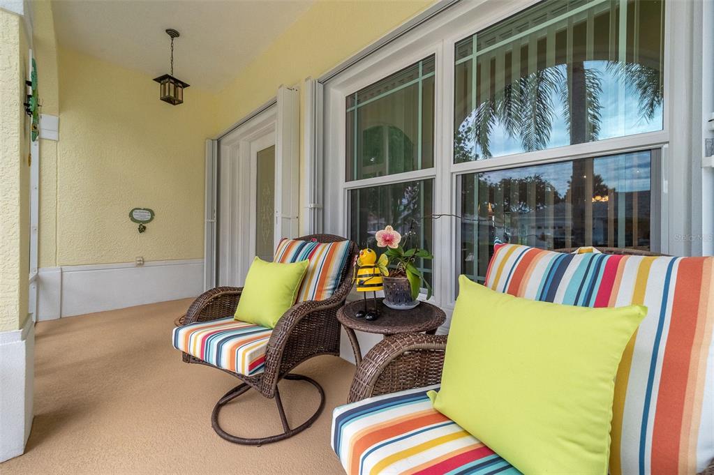 A covered patio features two wicker chairs with striped cushions and a small side table — 411 WENTHROP CIRCLE, ROCKLEDGE, FL